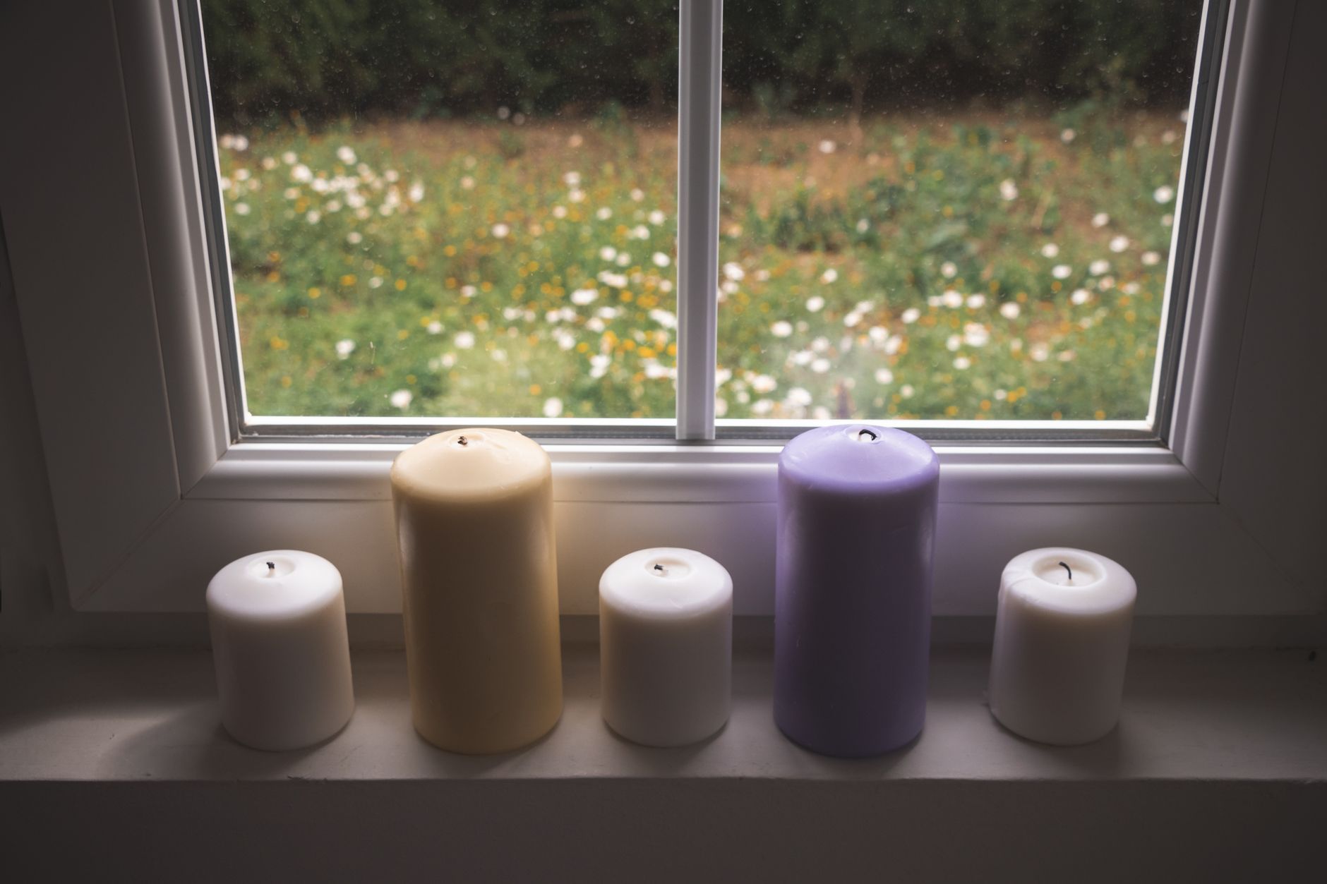 A serene view of colorful candles on a windowsill overlooking a garden. Perfect for relaxation themes.